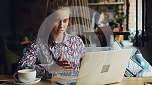 Cheerful young lady communicating with laptop skyping talking smiling in cafe