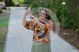 Cheerful young lady with glasses capturing a selfie in a lush green park