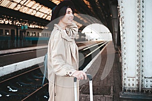 Cheerful young lady traveler is waiting for her train at the train station