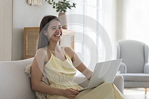 Cheerful young Latin woman using laptop on home sofa