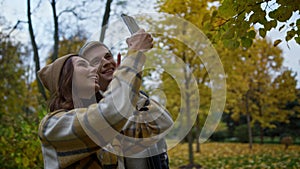 Cheerful young lovers making selfie video in autumn nature. Side shot.