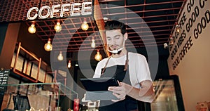 Cheerful young male cafe owner browsing for coffee recipes using digital tablet