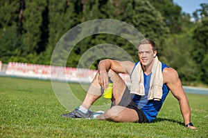 Cheerful young male runner is resting on grass