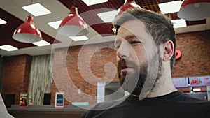 A cheerful, young man with a beard reads the menu and makes an order at the bar