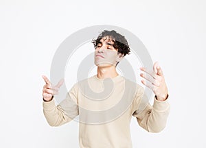 A cheerful young man in a beige sweater dances on a white studio background, enjoys life