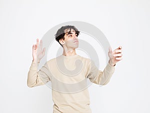 A cheerful young man in a beige sweater dances on a white studio background, enjoys life