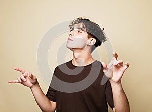 A cheerful young man in a brown t-shirt dances on a beige studio background, enjoys life