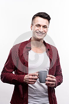 Cheerful young man in checked shirt holding cup of coffee