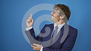 Cheerful young man in a crisp business suit confidently pointing aside with a hitchhiker\'s thumb, beaming a trustful smile on his
