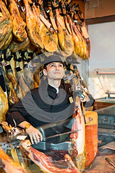 Cheerful young man cutting ham in jamoneria