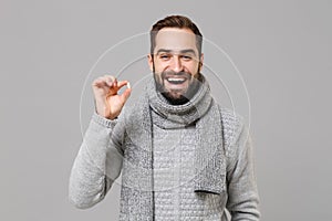 Cheerful young man in gray sweater, scarf isolated on grey wall background. Healthy lifestyle ill sick disease treatment