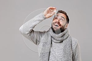 Cheerful young man in gray sweater, scarf isolated on grey wall background studio portrait. Healthy lifestyle, ill sick