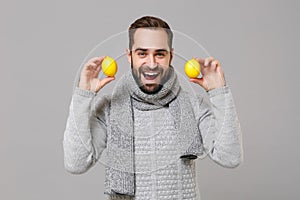 Cheerful young man in gray sweater, scarf posing isolated on grey wall background, studio portrait. Healthy fashion