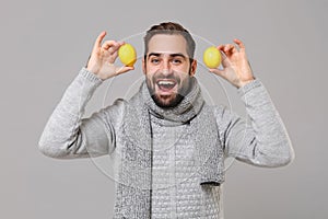 Cheerful young man in gray sweater, scarf posing isolated on grey wall background, studio portrait. Healthy fashion