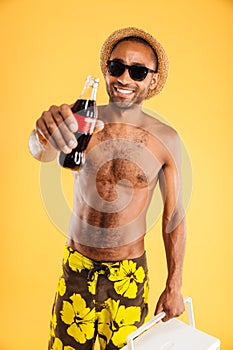 Cheerful young man in hat and sunglasses holding coke bottle