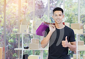 Cheerful young man holding colorful shopping bags, giving thumb up, and looking at the camera while standing in the office