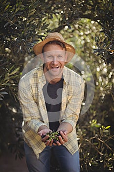 Cheerful young man holding olives while standing by trees at farm