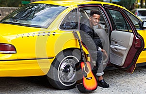 Cheerful young man in interior salon of car with openend door of yellow car, looking a side, near guitar.