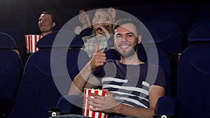 Cheerful young man showing thumbs up while watching movies at the cinema