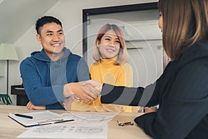 Cheerful young man signing some documents and handshaking with broker while sitting at desk.