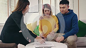 Cheerful young man signing some documents while sitting at desk together with his wife. Buying new house real estate.