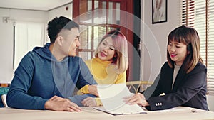 Cheerful young man signing some documents while sitting at desk together with his wife. Buying new house real estate.