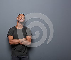 Cheerful young man smiling with arms crossed on gray background