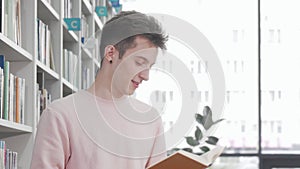 Cheerful young man smiling while reading a book at college library