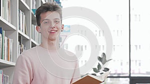 Cheerful young man smiling while reading a book at college library