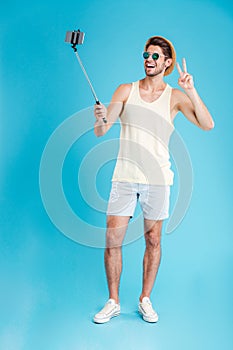 Cheerful young man taking selfie with smartphone and monopod