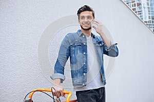 Cheerful young man talking on the mobile phone and smiling while standing near his bicycle
