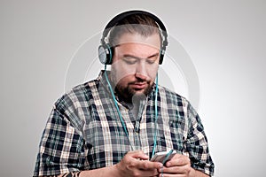 Cheerful young man using earphones and listening to music from mobile phone over grey background