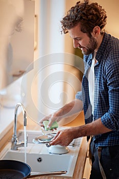 A cheerful young man washing dishes in the kitchen. Kitchen, housework, quarantin, home photo