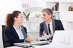 Cheerful young man and woman coworkers talking in firm office