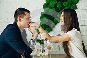 Cheerful young man and woman are dating in restaurant. They are sitting at the table and looking at each other with love