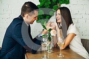 Cheerful young man and woman are dating in restaurant. They are sitting at the table and looking at each other with love