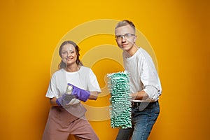 Cheerful young man and woman standing on orange studio wall background, cleaning service and housekeeping concept
