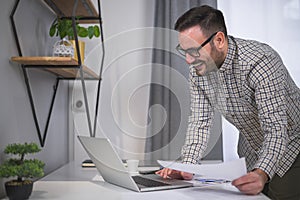 Cheerful young manager looking at his computer satisfied with the analysis of his latest business results