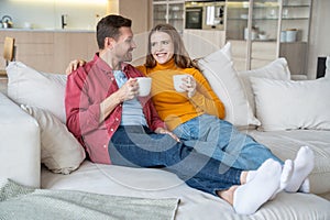 Cheerful young married couple spending pastime at home drinking tea, chatting, enjoying each other