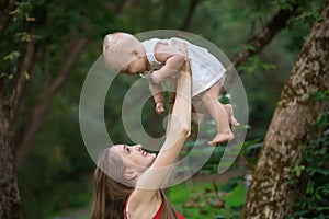 Cheerful young mother raises the baby in her arms. Happy motherhood and childhood