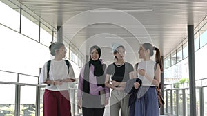 Cheerful young multi-racial Asian women students talking, laughing and walking in college hall.