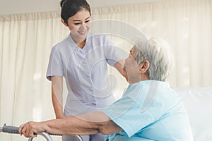Cheerful young nurse in homecare helping senior patient use walker to recovery from hip injury