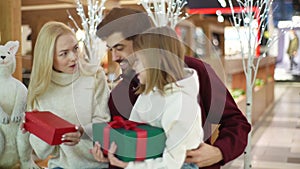 Cheerful young parents give gifts to daughter in shopping mall spending weekend together, standing on background of