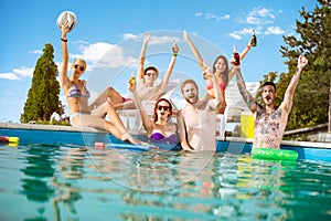 Cheerful young people in pool rejoice with raising hands with be