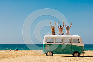 Cheerful young people relaxing on top of retro bus near sea