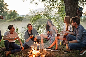 Cheerful young people warming near the camp fire