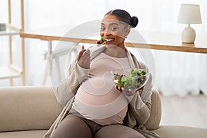 Cheerful young pregnant african american woman eating salad