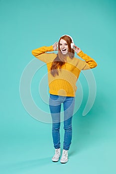 Cheerful young redhead girl in yellow knitted sweater posing isolated on blue turquoise background studio portrait