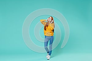 Cheerful young redhead girl in yellow knitted sweater posing isolated on blue turquoise background studio portrait