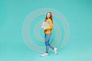 Cheerful young redhead girl in yellow knitted sweater posing isolated on blue turquoise wall background studio portrait